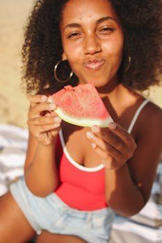 Happy woman enjoying a fresh slice of watermelon on a sunny summer day at the beach.