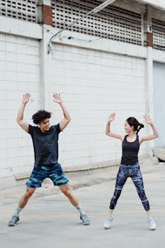 Energetic couple doing jumping jacks outdoors, showcasing fitness and active lifestyle.