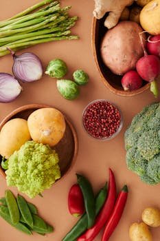 A colorful flat lay of fresh vegetables including asparagus, broccoli, and chili peppers on a brown surface.