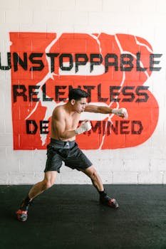Shirtless male boxer practicing shadowboxing in a gym with motivational graffiti on the wall.