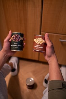 Close-up of hands holding canned red kidney and white beans indoors.